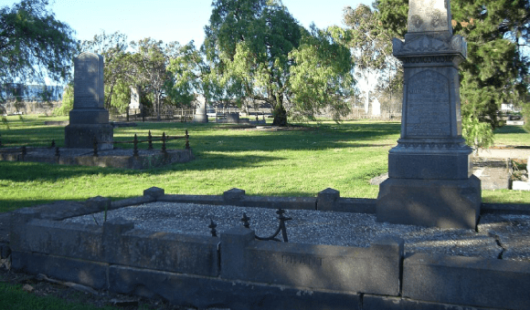 A neatly manicured lawn with gravestones and trees